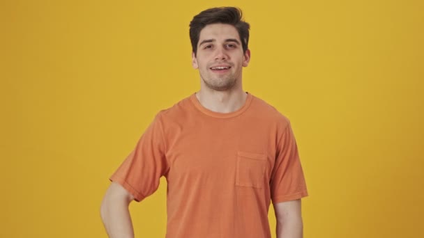 Happy handsome man wearing in t-shirt showing thumbs up gestures at the camera over yellow background - Metraje, vídeo