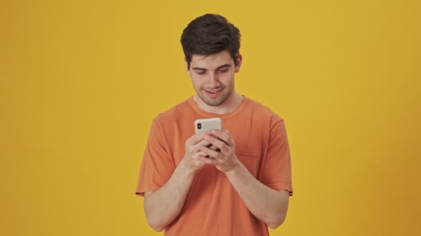 Bearded handsome man wearing in t-shirt using smartphone over yellow background - Video