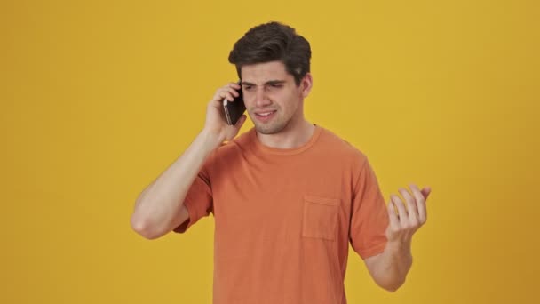Serious handsome man wearing in t-shirt talking by smartphone over yellow background - Кадры, видео