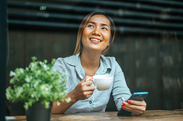 junge Frau sitzt in einem Café und spielt Smartphone - Foto, Bild