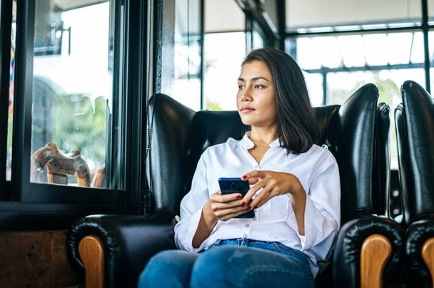 femme portant des vêtements blancs et assis jouer smartphone - Photo, image