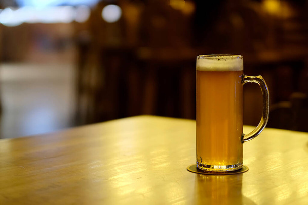 バーの木製の光沢のあるテーブルの上でビールを1杯閉じます。ぼかしの背景 - 写真・画像