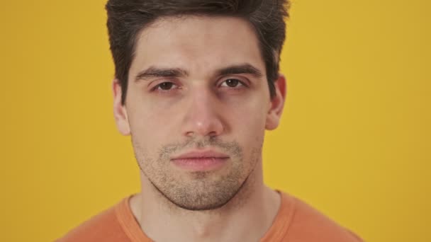 Close up view of Calm handsome man wearing in t-shirt open his eyes and looking at the camera over yellow background - Video