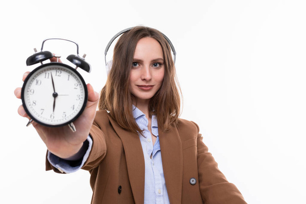 Una ragazza in giacca e cravatta marrone tiene un orologio che mostra la fine della giornata lavorativa sul posto di lavoro. Isolato - Foto, immagini