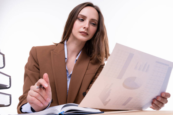 Ruskeassa puvussa oleva tyttö tarkistaa yhtiön kaaviot työpöydällä. Eristetty - Valokuva, kuva