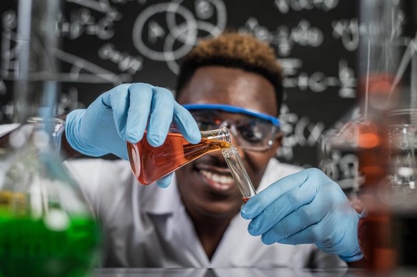 Gli scienziati mescolano sostanze chimiche rosse e arancioni in un bicchiere al laboratorio. - Foto, immagini
