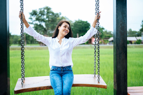 Woman sitting on a swing and holding her hand at the chain - Photo, Image