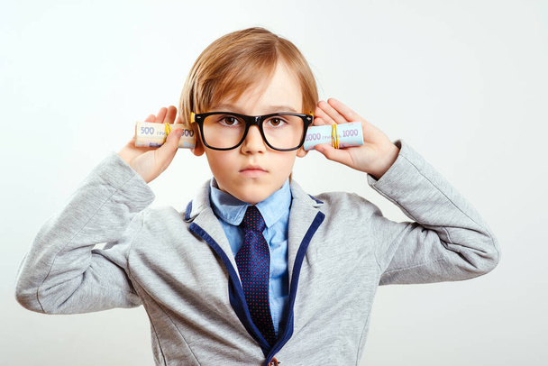 Financial education for children. Smart boy with rolls of money. Little successful businessman on white background. Financial monitoring of currency. Future profession. Little boss in eyeglasses and suit. - Photo, Image