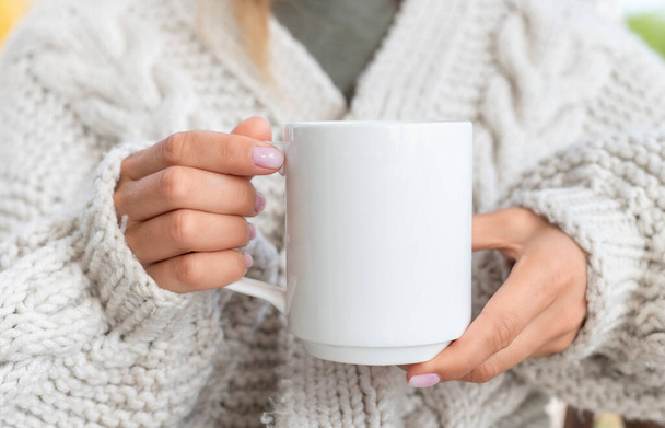 Weiße Keramikbecher-Attrappe vorhanden. Frau im Pullover hält eine warme Tasse Kaffee in der Hand. Kopierplatz für Ihren Druck - Foto, Bild
