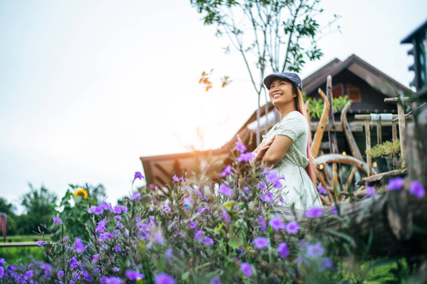 Женщина счастливо стоит в цветочном саду на деревянных перилах. - Фото, изображение