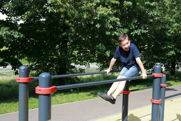 Boy trains abdominal muscles on uneven bars in park - Fotó, kép