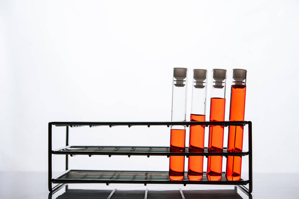 Πορτοκαλί χημικές ουσίες σε ένα σωλήνα από γυαλί επιστήμης τοποθετημένα σε ένα ράφι. - Φωτογραφία, εικόνα