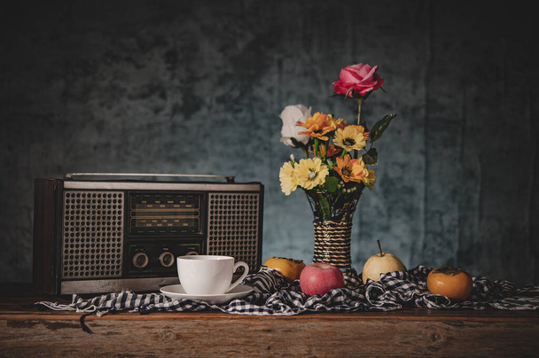 Natureza morta com vasos, flores, frutas, xícaras de café e um receptor de rádio retro
. - Foto, Imagem