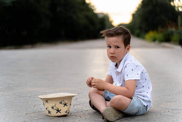 a sad boy sits on the ground and asks - Φωτογραφία, εικόνα