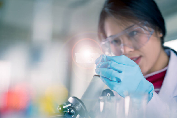 Jeune technologue médical asiatique femelle faire des tests avec éprouvette tout en faisant de la recherche dans un laboratoire scientifique - Photo, image