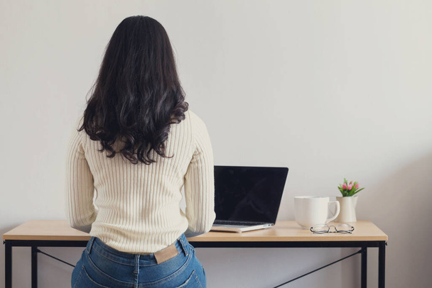 Πίσω πλευρά των νεαρών ευτυχισμένων Ασιάτισσων γυναικών που εργάζονται στο φορητό υπολογιστή της στο γραφείο στο σπίτι. - Φωτογραφία, εικόνα