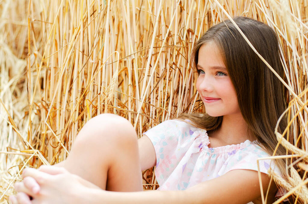 Portrait of smiling cute little girl child sitting on field of wheat outdoor - Foto, afbeelding