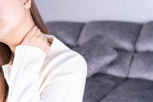 Junge Frau leidet unter Nackenschmerzen, während sie zu Hause auf dem Sofa sitzt. Gesundheitswesen medizinisches oder tägliches Lebenskonzept. - Foto, Bild