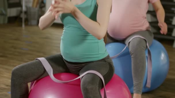 Dengeli topların üzerinde oturan iki hamile kadının çekimini yukarı kaldır ve fitness dersinden önce ısınma egzersizleriyle ısınmaya başla. - Video, Çekim