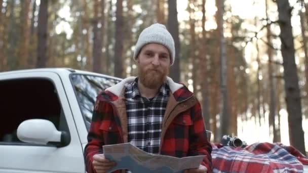 Portret van een jonge gemberharige man met baard die bij een crossover auto staat, papieren man vasthoudt en lacht naar de camera, medium shot - Video