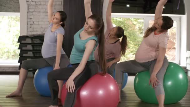 ジムで安定したボールに座っている4人のアクティブな妊婦のグループと彼らのトレーナーとストレッチ練習を実行します。 - 映像、動画