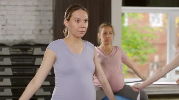 Dengeli topların üzerinde oturan ve spor yaparken bantla omuz daireleri yapan dört aktif hamile kadının orta boy fotoğrafı. - Video, Çekim