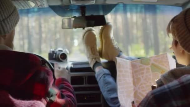 Vista trasera de la joven pareja caucásica viajando en coche, hombre sentado en el asiento del conductor y mujer usando el mapa y hablando con él
  - Metraje, vídeo