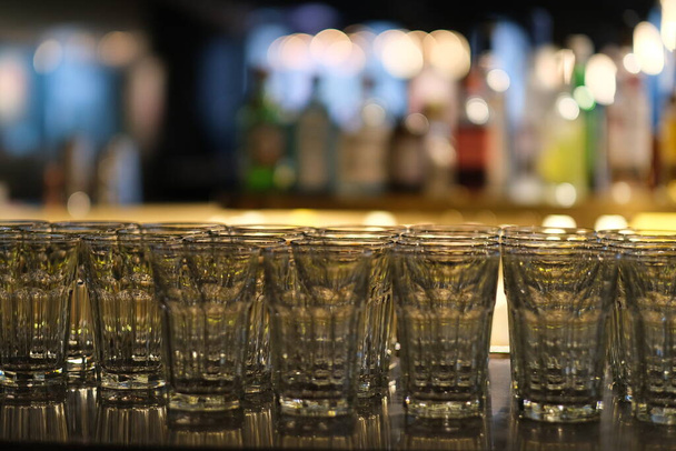 close up lots of empty drinking glasses on bar counter. colorful bokeh background - Photo, image