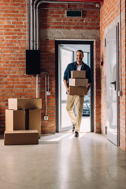 χαρούμενος επιχειρηματίας κρατώντας κουτιά χαρτοκιβωτίων, ενώ κινείται στο νέο γραφείο  - Φωτογραφία, εικόνα