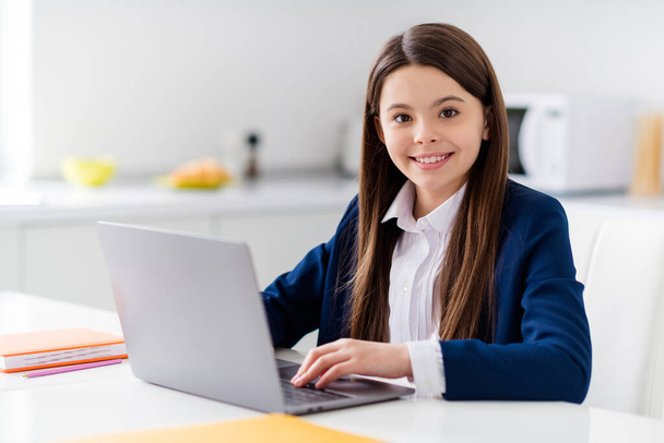 Photo of little cheerful pretty student girl diligent student notebook online lesson video call sit desk distance quarantine study september at home living room house classroom indoors - Foto, afbeelding