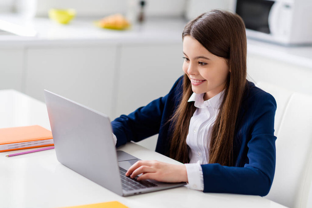 Photo of little pretty student school girl diligent student notebook online lesson video call sit desk distance quarantine study september at home living room house classroom indoors - Foto, Imagen