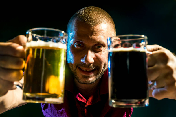 Satisfied man with light and dark beer in mugs on a dark green background - Foto, imagen