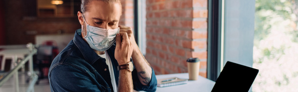 panoramic crop of businessman wearing medical mask near laptop with blank screen  - Photo, image