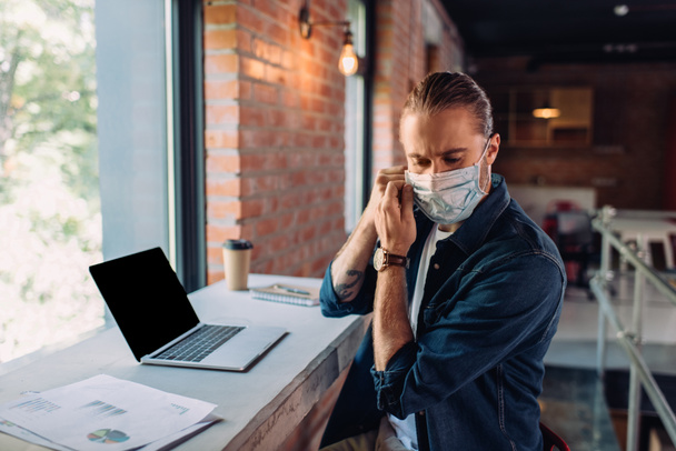 businessman wearing medical mask near laptop with blank screen  - Photo, Image