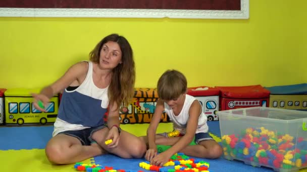 Pequeño hijo con mamá juega constructor en el rompecabezas de la alfombra en la sala de juegos
. - Imágenes, Vídeo