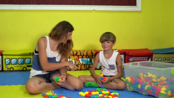 Piccolo figlio con mamma gioca costruttore sul puzzle tappeto nella sala giochi. - Filmati, video
