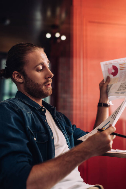 selective focus of handsome and bearded businessman looking at charts and graphs  - Fotoğraf, Görsel
