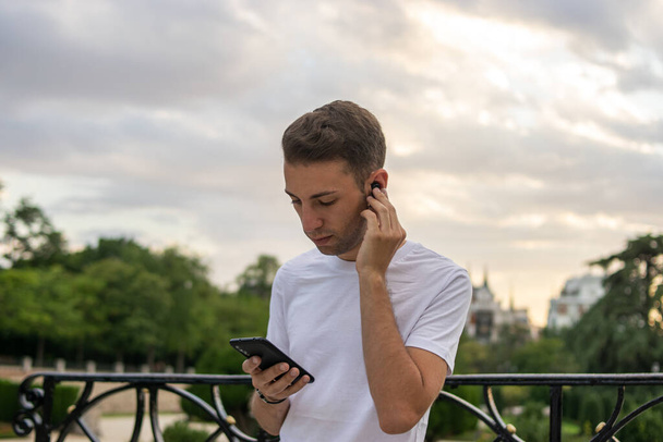 Foto de um homem jovem e atraente com fones de ouvido ouvindo música em seu telefone no parque - Foto, Imagem