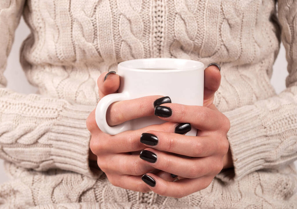 Női kéz fekete körmökkel és pulóver tartó csésze tea, közelről - Fotó, kép