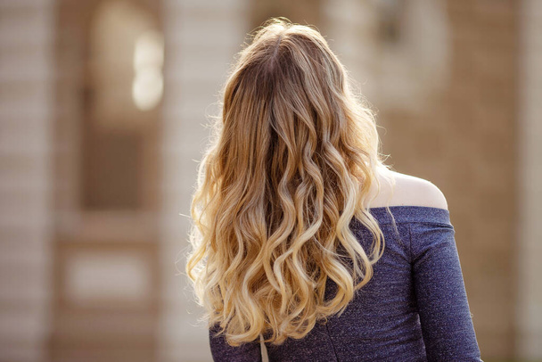 Fashion outdoor photo of beautiful young woman. View from a back. Close up picture. Beautiful streaming blonde curls. Copy space - 写真・画像