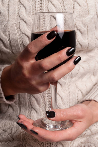Weinglas in jungen Frauenhänden mit schwarzen Nägeln und Pullover, Nahaufnahme - Foto, Bild
