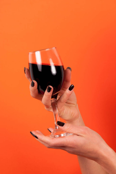Wine glass in women hand with black nail isolated on orange background, close up - Photo, Image