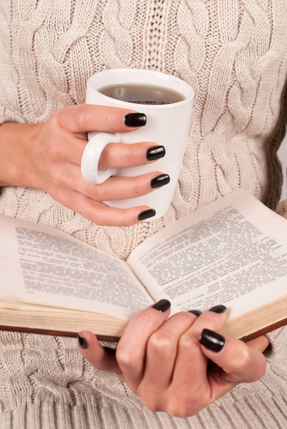 Teekuppi ja kirja nuorille naisille kädet mustat kynnet ja pusero, lähikuva - Valokuva, kuva