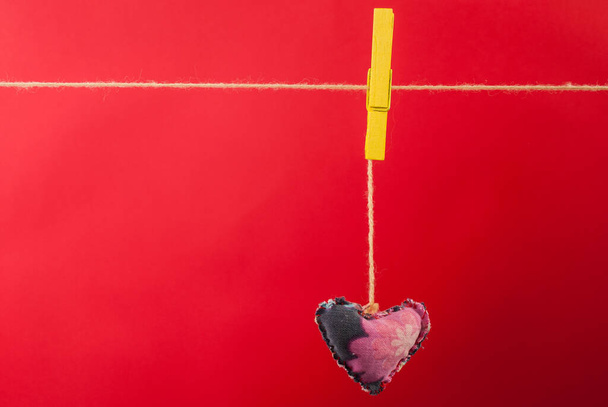 Heart fabric hanging on clothesline and red background with free space - Foto, imagen
