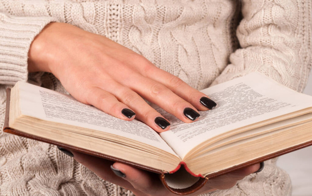 Junge Mädchenhand mit schwarzen Nägeln hält Buch, Frau im Pullover liest Buch, Nahaufnahme - Foto, Bild