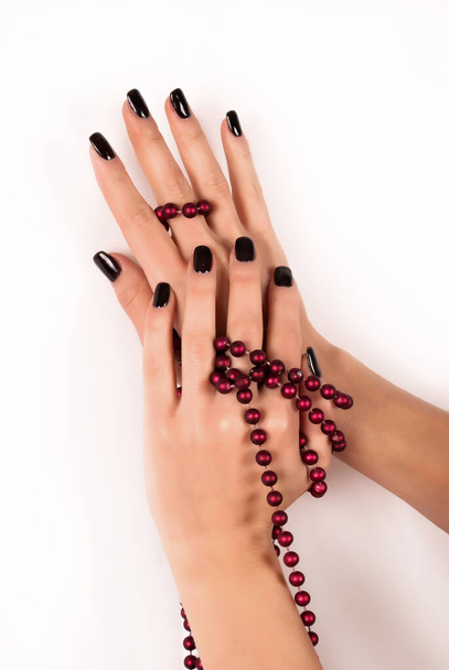 Frauenhände mit schwarzen Nägeln und roter Perlenkette auf rotem Hintergrund, Nahaufnahme - Foto, Bild