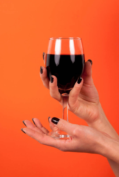 Female holding wine glass in hands with black nails isolated on orange background, close up - Photo, Image