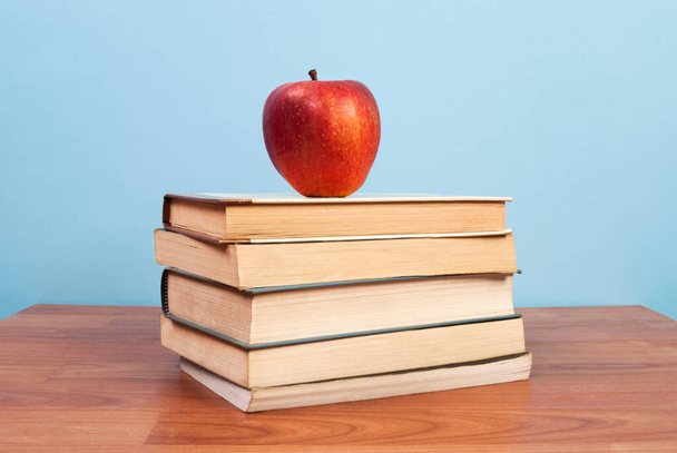 Apple on books placed on a wooden table and background is blue - Foto, imagen