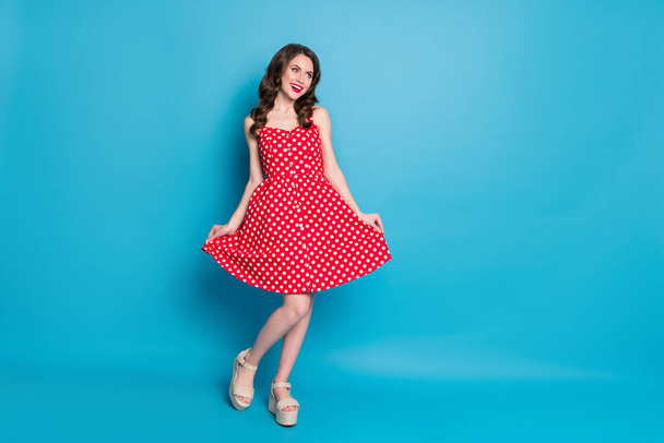 Full length photo of attractive lady shiny pomade smiling toothy flirty hold skirt shy look empty space wear red white dotted retro dress summer open toe shoes isolated blue color background - Фото, изображение