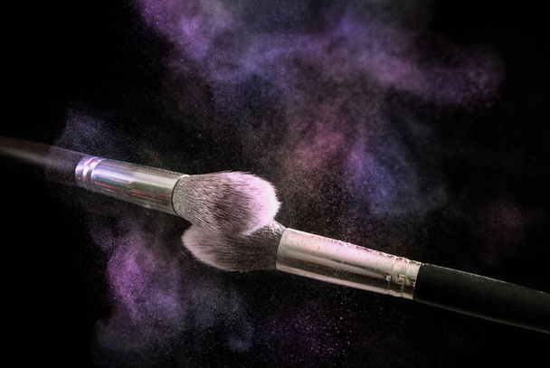 Two make up brushes with colorful powder explosion dust cloud, selective focus, close up - 写真・画像